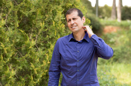 Man suffering itching scratching neck standing outdoors in a parkの写真素材
