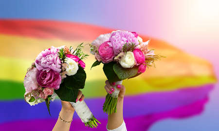 Lesbians in wedding holding a bouquet of flowers celebrating the wedding against the LGBT flagの写真素材