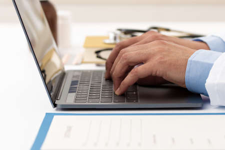 Shot of an unrecognizable male doctor working on his laptop while sitting in his office at hospitalの写真素材