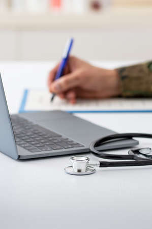 Closeup shot of a stethoscope resting on a laptop with an unrecognizable army doctor workingの写真素材