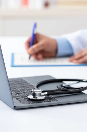Closeup shot of a stethoscope resting on a laptop with an unrecognizable doctor workingの写真素材