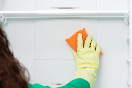 Female hand cleaning refrigerator door with scourer at home