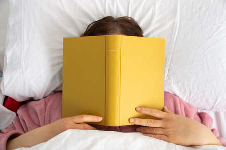 Woman sleep on bed with book cover his face, sleep late reading book prepare for exam.の写真素材