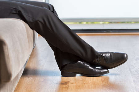 Profile of a tired businessman legs with suit sitting on couch at home after workの写真素材