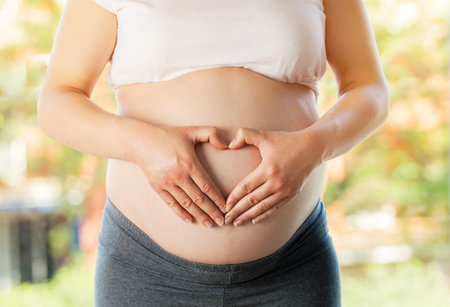 Cropped shot of a pregnant woman touching her belly on a light natural background