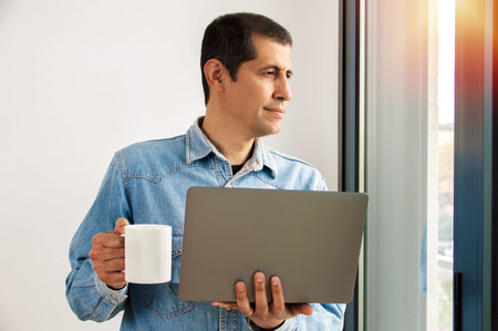 Shot of a handsome young businessman drinking coffee while working on a laptop in his home office...
