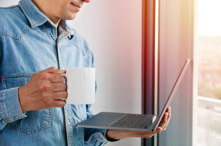 Shot of a handsome young businessman drinking coffee while working on a laptop in his home office
