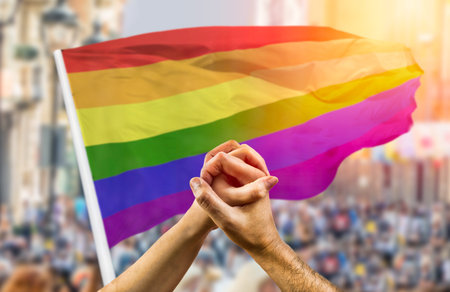 Cropped shot of a couple holding hands and wave in front of a rainbow flag flying on the sidelines...