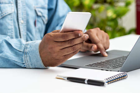 Close up of a man hands using a smart phone and a laptop on a desktop at home or officeの写真素材