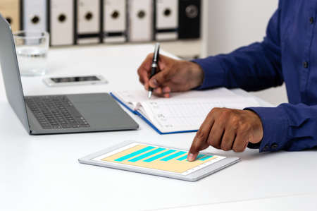 Shot of an unrecognizable businessman using a digital tablet with graphs on it in a modern officeの写真素材