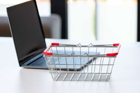 Laptop and small shopping cart on table. Internet shopping conceptの写真素材