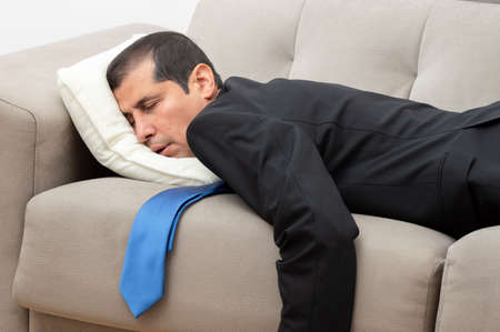 Tired businessman sleeping lying on a sofa in the living room at home after workの写真素材