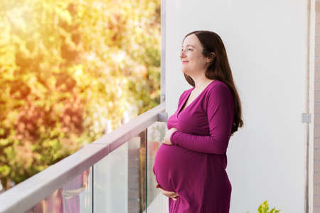 Side view portrait of a pensive pregnant woman looking away in a house balcony at sunsetの写真素材
