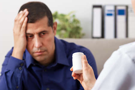 A male doctor giving a bottle of pills to one of his patients during a checkup with focus on the bottleの写真素材