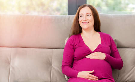 Portrait of a happy pregnant woman rests at home looking to the right at living roomの写真素材