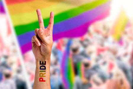 Supporting hand makes peace sign in front of a rainbow flag flying on the sidelines of a summer gay pride parade with copy spaceの写真素材