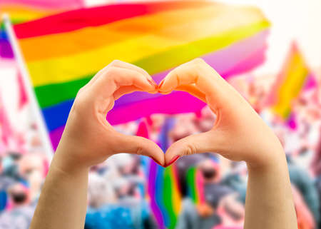 Supporting hands make heart sign and wave in front of a rainbow flag flying on the sidelines of a summer gay pride paradeの写真素材