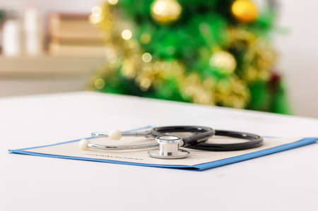 Close-up of a stethoscope and a doctor's notebook on a table in the hospital with a christmas tree in the backgroundの写真素材