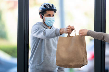 Shot of a masked man delivering a food package at home with focus on the hand and copy spaceの写真素材