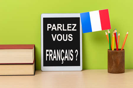 A digital tablet with the question parlez-vous francais? do you speak french? written in french, a pot with
pencils and the flag of France, on a wooden desk with green backgroundの写真素材