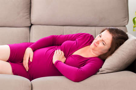 Shot of a pregnant woman suffering belly ache lying on a couch at homeの写真素材