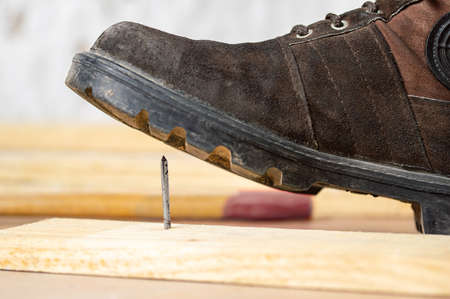 Close-up of man's foot stepping over there nail inserted in wooden plank.Home safety conceptの写真素材