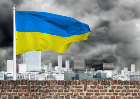 Ukrainian flag on a brick wall of a building. Ukrainian flag in the sky of storm black clouds.の写真素材