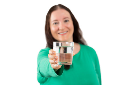 Beautiful woman smiling while holding a glass of water with white background. Lifestyle concept.の写真素材