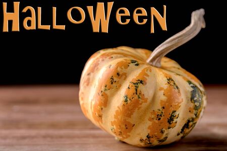 small decorative pumpkin isolated on wood with halloween writtenの写真素材