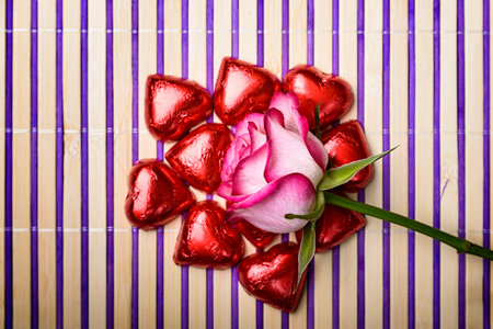 white and pink rose on wrapped chocolate heart on striped background Wooden and purple