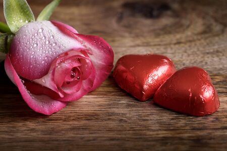 roses and two heart-shaped chocolates on woodの写真素材