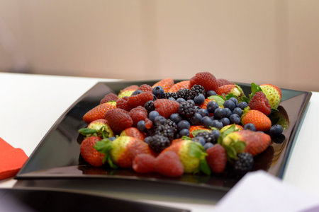 black plate full of fresh fruit on white tableの写真素材