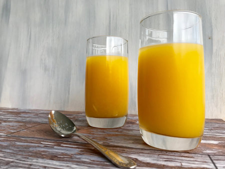 Two glasses of orange juice for breakfast with spoon