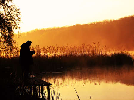 Silhouette of the fisherman on lake in rising sun beamsの写真素材