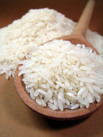Rice grains in a wooden spoon on a brown backgroundの写真素材