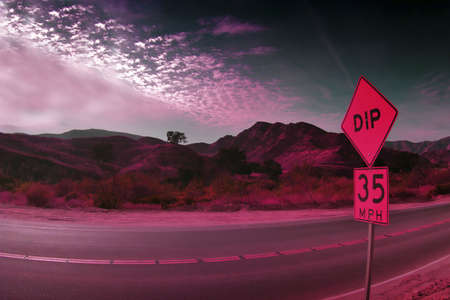 Desert in pink light with speed limit street sign and rocky mountains in the backgroundの写真素材