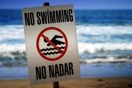 no swimming sign on a beach with waves in the background