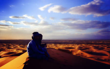 two people sitting on top of a dune looking at the spectacular Sahara desertの写真素材