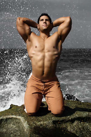 Bodybuilder on beach with ocean spray behind himの写真素材