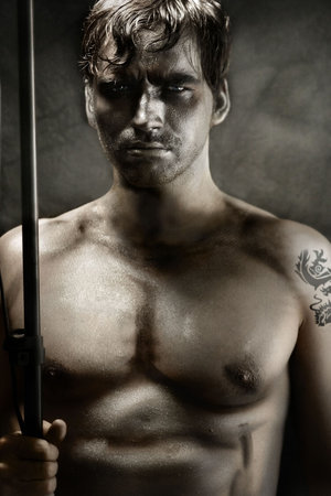 Classically styled portrait of a shirtless young man portraying a tribal warrior with spearの写真素材