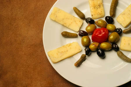 Plate of gourmet cheese, olives, and pickles on rustic brown table の写真素材