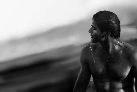 Fine art black and white portrait of young beautiful naked man in the ocean with water dripping off his bodyの写真素材