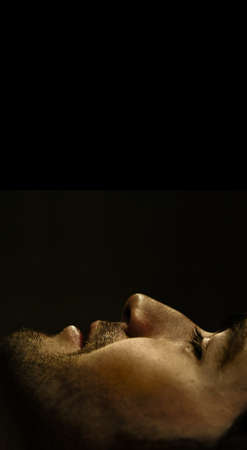 Dramatic close-up profile portrait of young man's face at the bottom of frame against black background and lots of top copy spaceの写真素材