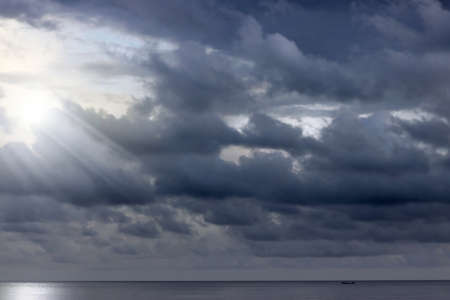 Ominous clouds above the ocean with rays of light peaking throughの写真素材