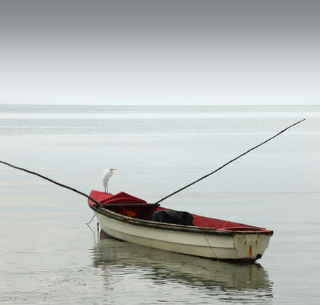 A lonely rowboat on calm seas against moody grey skyの写真素材