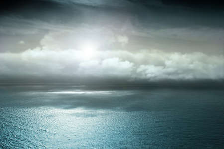 Landscape photo of a still sea and a beautiful moody sky with sun behind cloudsの写真素材