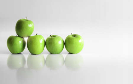 Five shiny green apples in empty white reflective spaceの写真素材