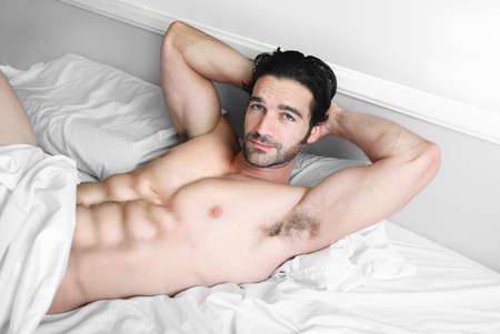 Young muscular male model lying back in bed with sexy smileの写真素材