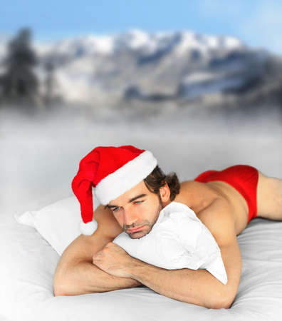 Hunky male santa laying in bed on pillow with winter snow backgroundの写真素材