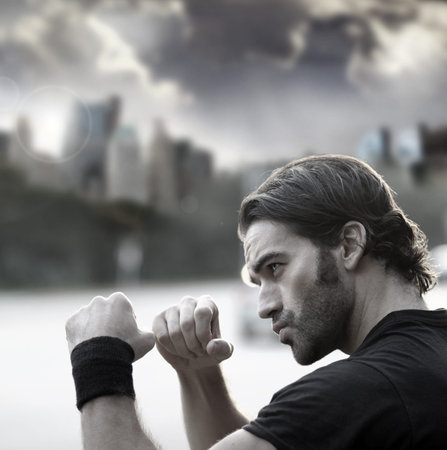 Retro styled photo of a young sexy man with fists up ready to fight against city background and...